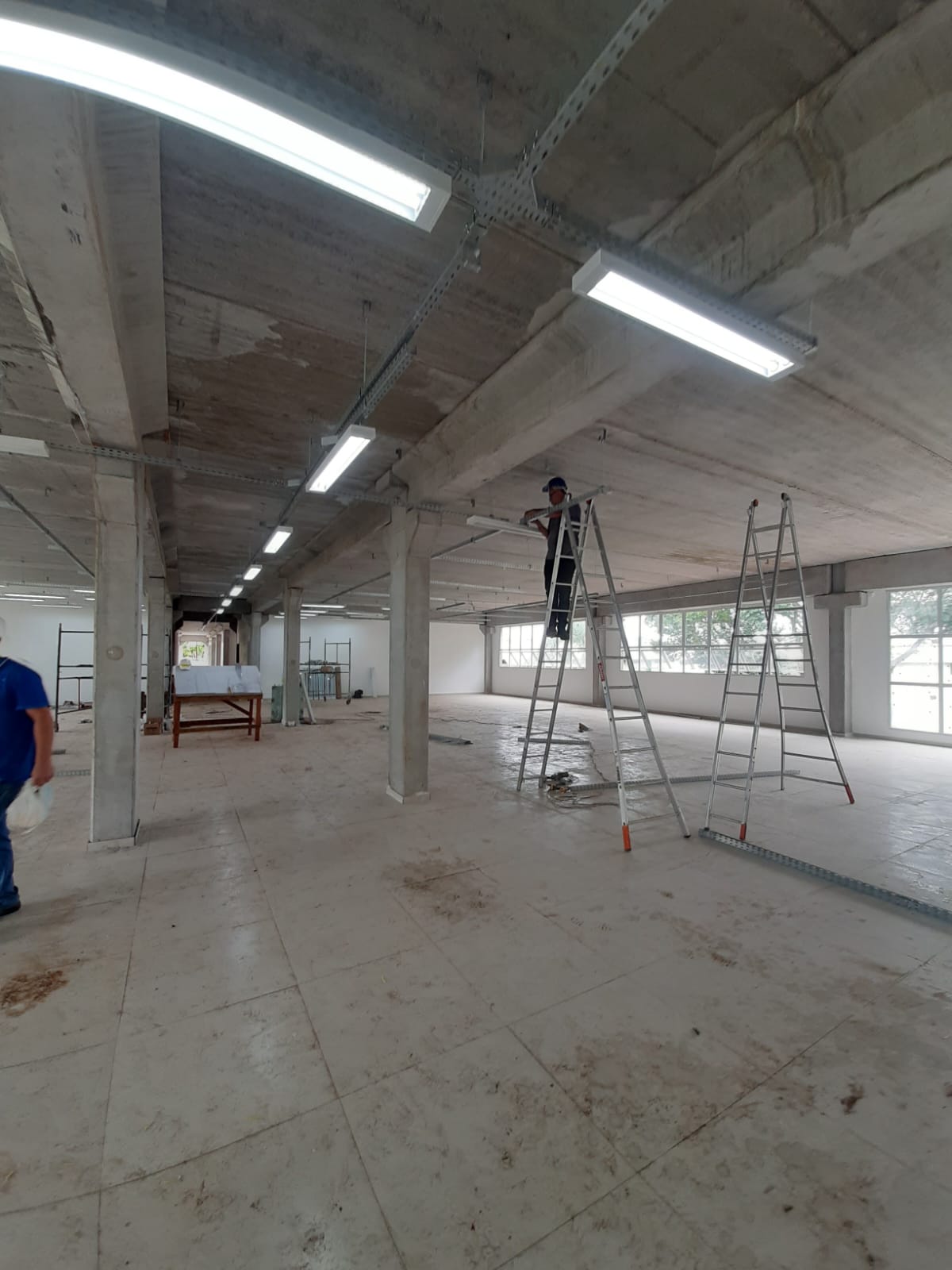 Equipe executando instalação de iluminação e eletrocalhas em amplo espaço comercial